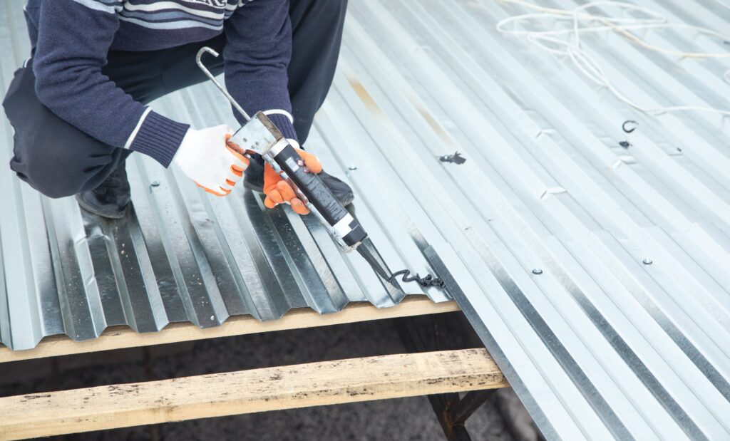 Technician applying sealant on metal roofing sheet, completing durable new roof installation work