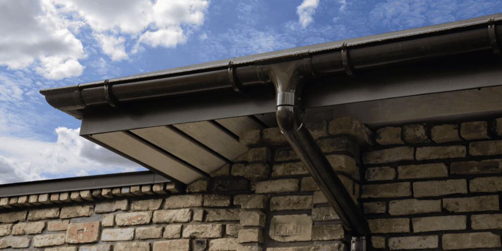 Brown vinyl gutter material and downspout on brick building corner showcasing durable gutter types