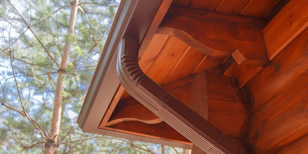 Gutter replacement on a wooden roof edge with new brown downspout installed to protect the home from rainwater