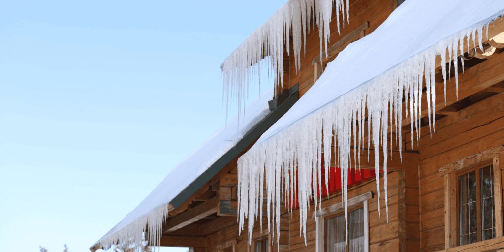 Heavy ice dams hanging from a snowy roof, with thick icicles that signal trapped meltwater and cold weather risk