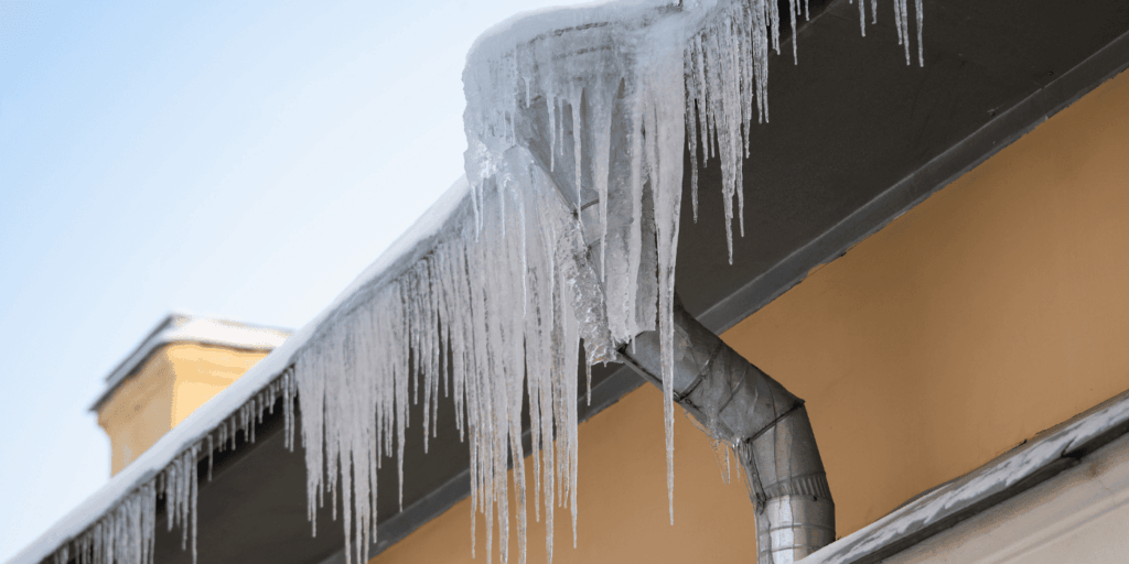 Large ice dams along the gutter line, creating frozen runoff that may lead to roof leaks and wood damage