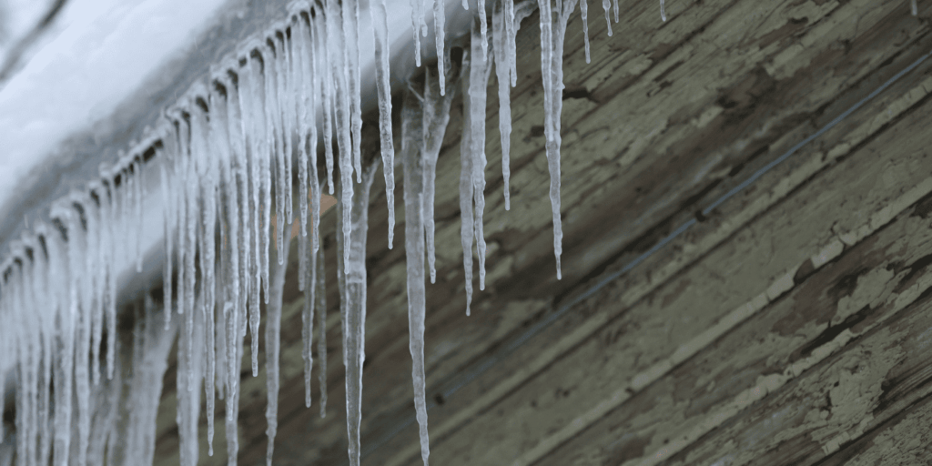 Ice dams forming along roof edge with long icicles, showing winter buildup that can block drainage and cause damage