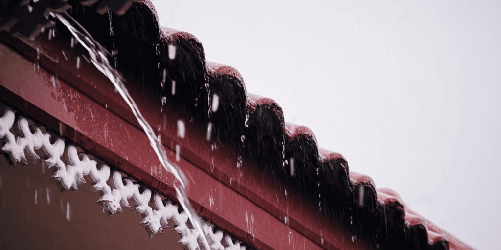 Rainwater pouring over roof tiles and fascia, showing a roof leak caused by damaged roofing materials