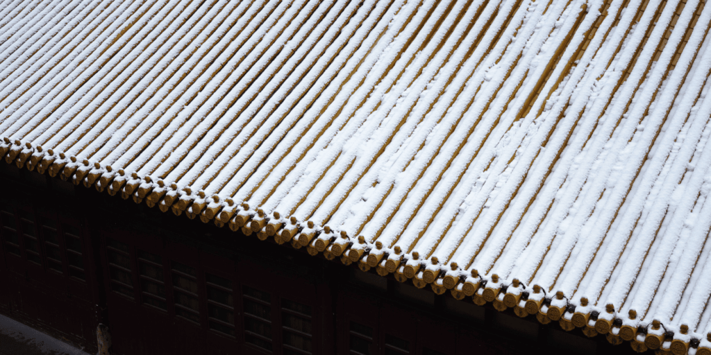 Close view of a tiled roof with light snow, reminding homeowners about regular roof care in winter