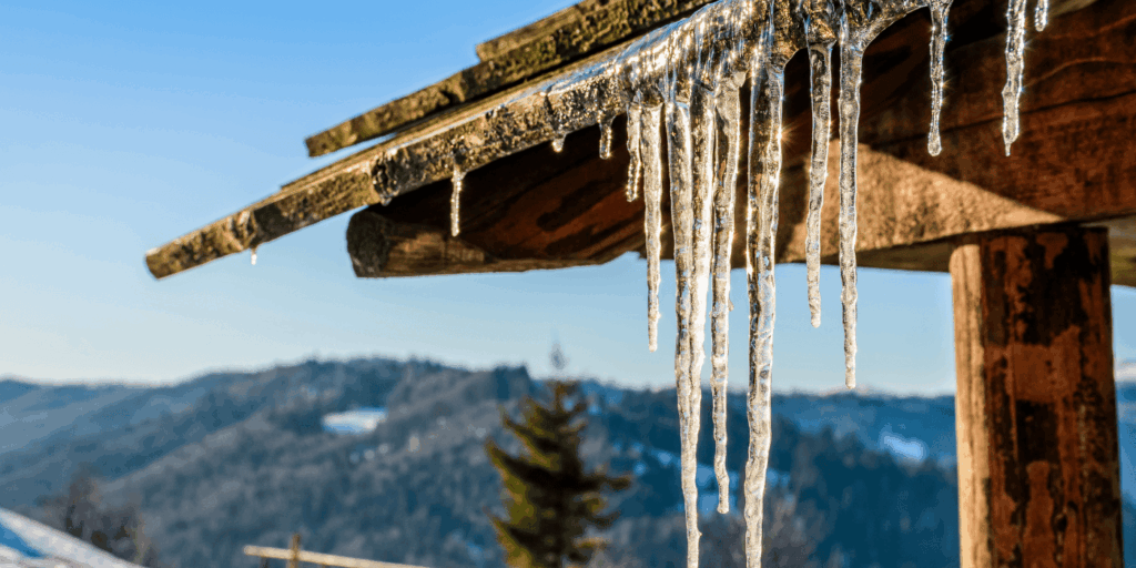 Ice dams hanging from a roof edge on a cold day, a common sign that roof care in winter is needed