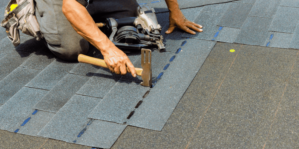 Contractor performing roof repair by securing asphalt shingles with a hammer during a residential roofing installation.