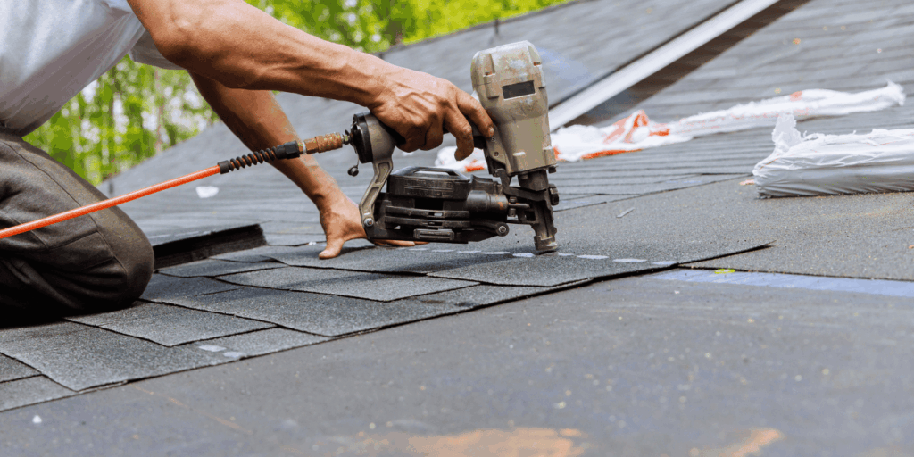 Professional roof repair in progress as a roofer installs new asphalt shingles using a nail gun on a residential roof.