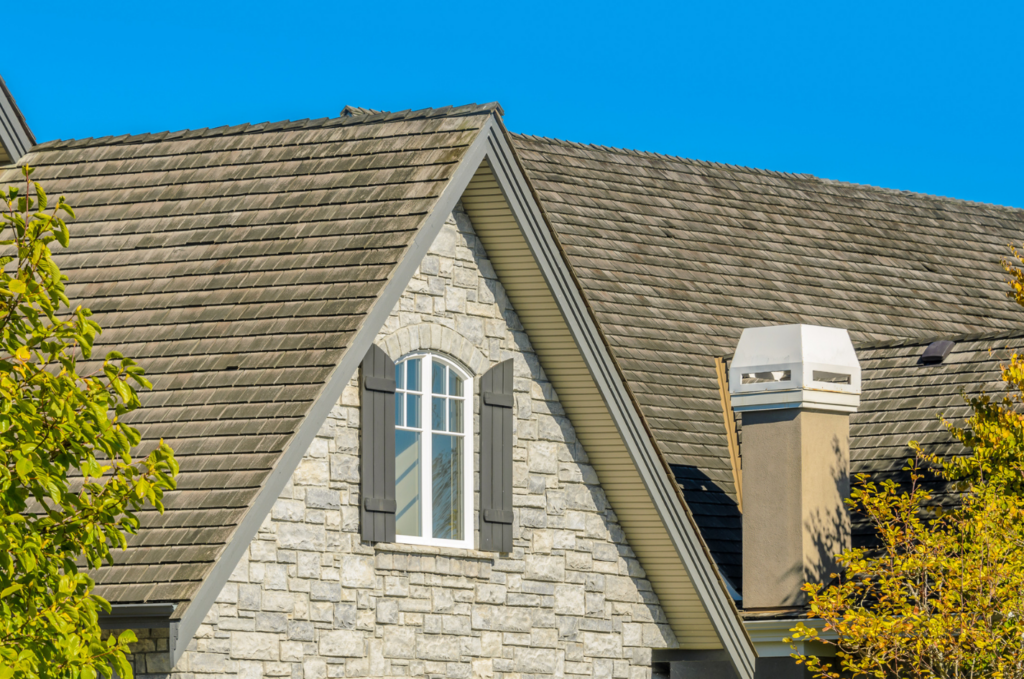 Clean residential home roof after roof repair, featuring well-aligned shingles, stone exterior wall, and chimney under a clear sky
