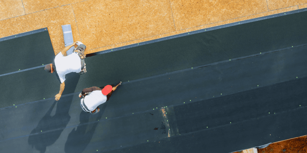 Roofing team installing layered flat roof materials designed to create a smooth, durable, and waterproof roofing system.