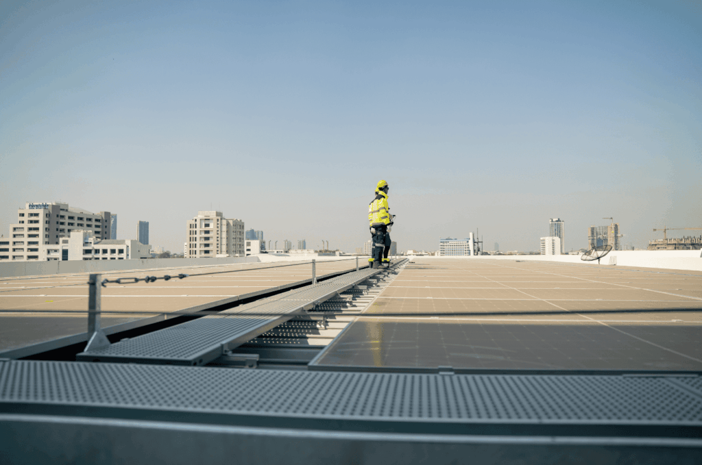 Worker walking on a commercial roof with solar panels, checking the surface and equipment for safety and performance