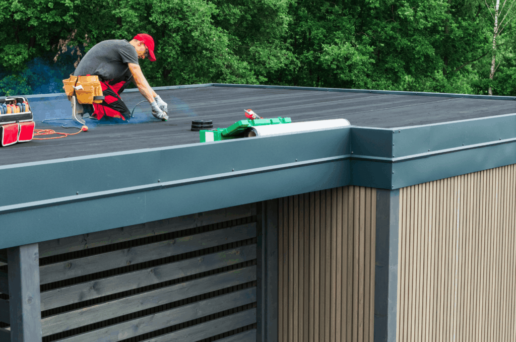 Worker installing rubber roofing on a flat roof, carefully sealing edges to protect the building from leaks and weather.