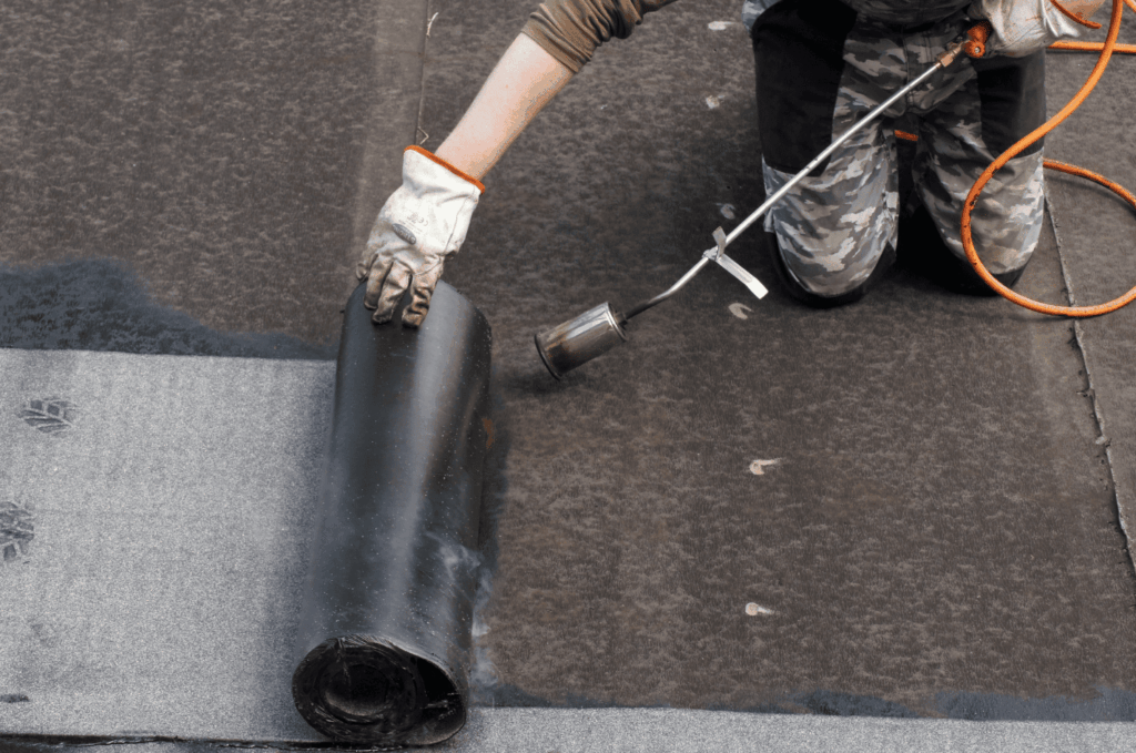 Roofing professional rolling out rubber roofing membrane and heating it to create a durable, watertight surface
