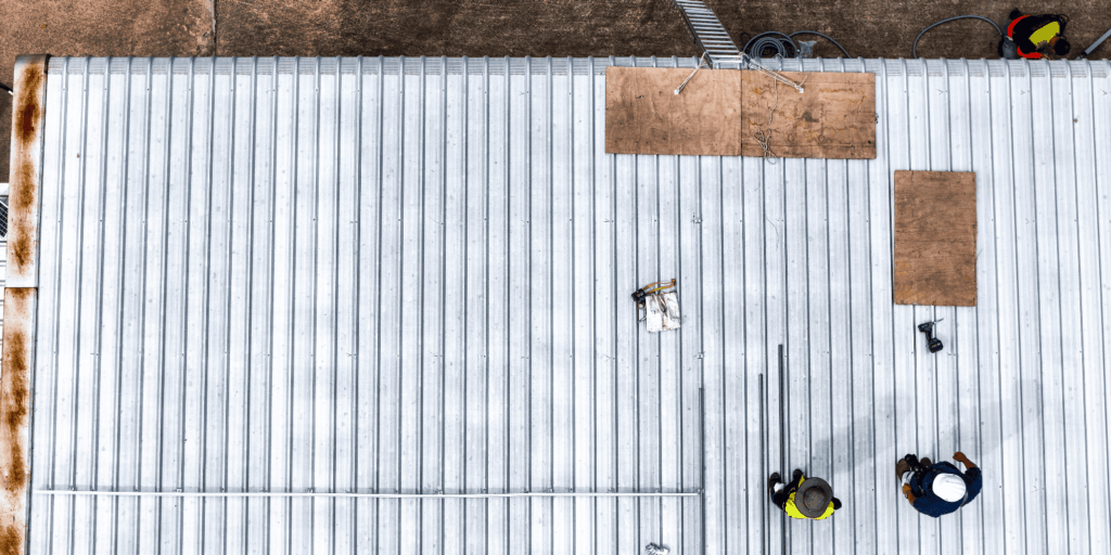 Top view of a metal commercial roof with workers inspecting materials and preparing the surface for maintenance work