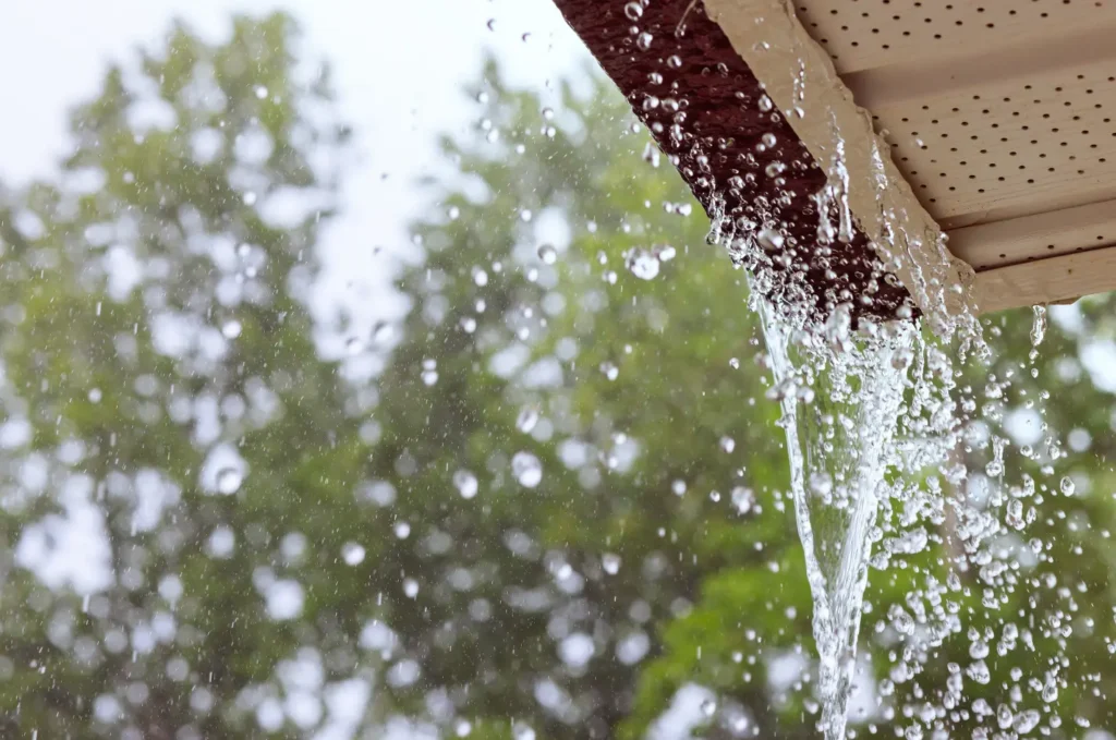 Heavy rain pouring from a damaged gutter edge, showing signs of a roof leak during a severe storm