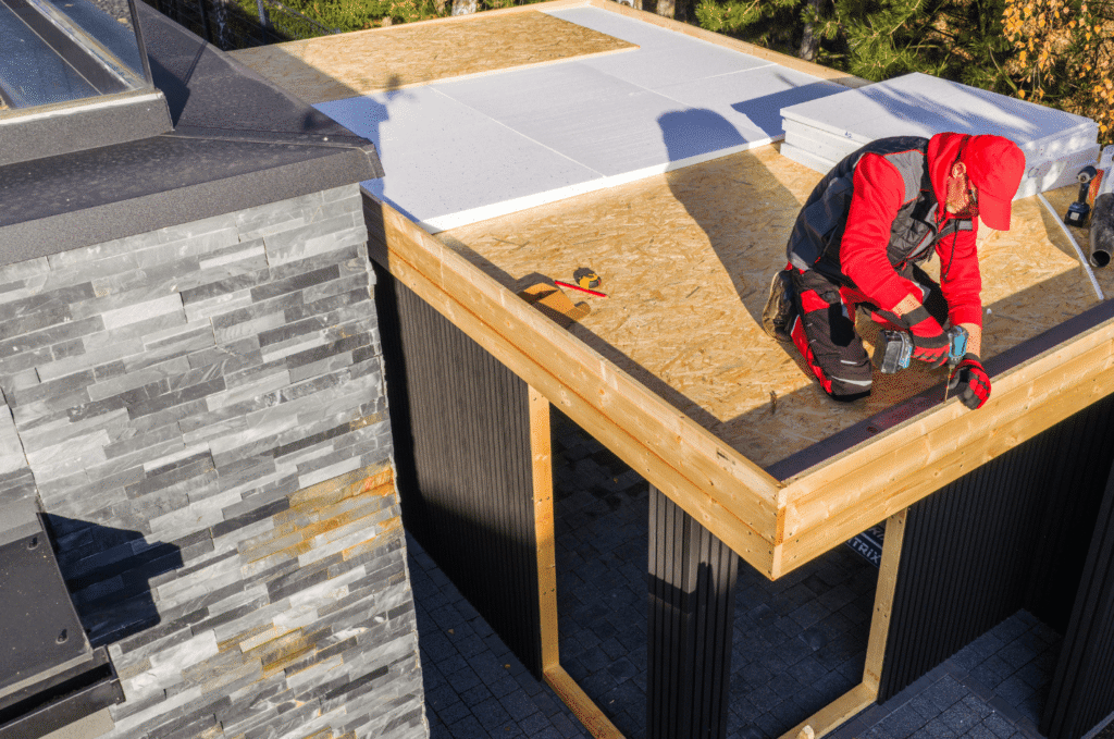 Worker completing a roof installation on a flat roof extension using wood framing and weatherproof materials