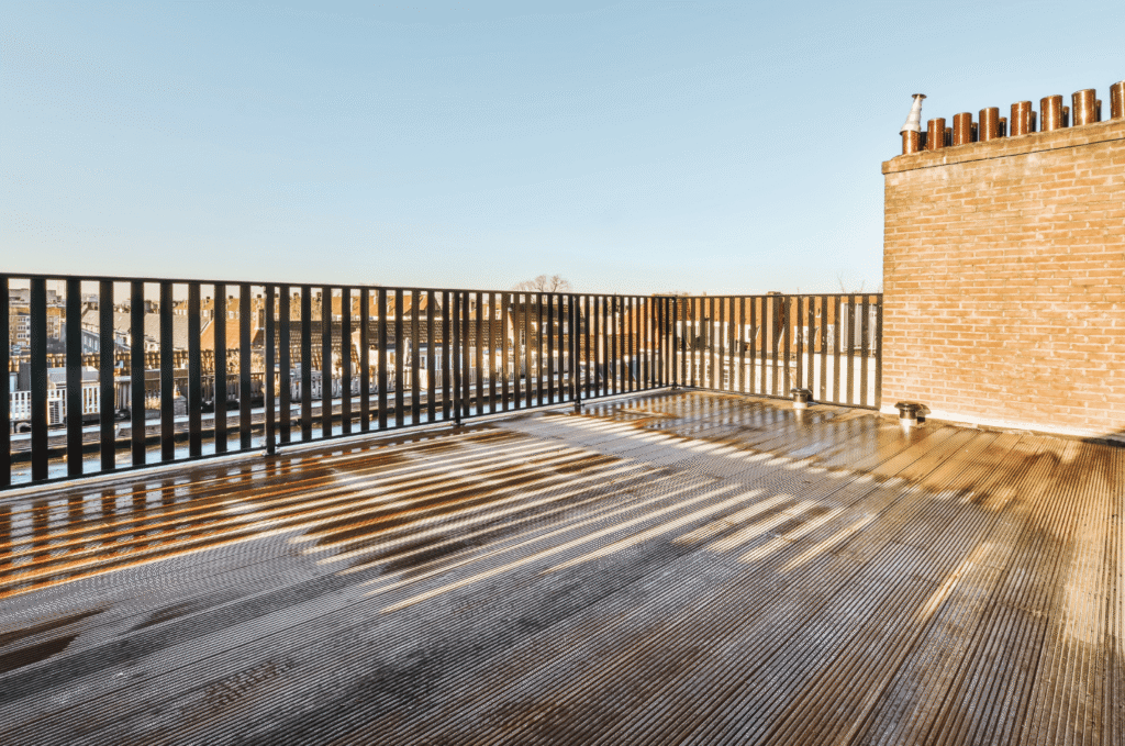 Finished roof deck install with wooden flooring, safety railing, and open city views on a sunny afternoon
