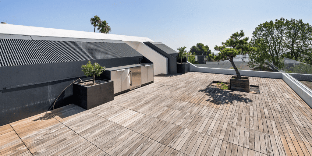 Spacious roof deck install with wood tile flooring, outdoor kitchen area, and decorative plants on a rooftop