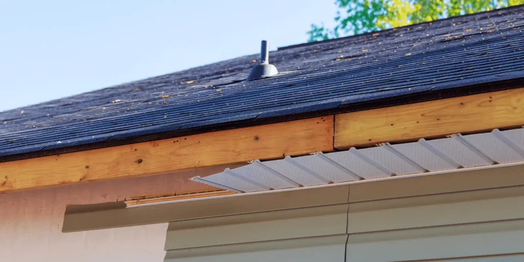 Close view of roof flashing and soffit installation beneath dark roof shingles on a residential home exterior