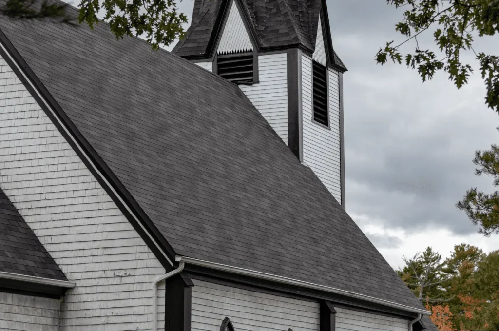Church building with a steep shingle roof showing durable emergency roofing support during storm recovery work